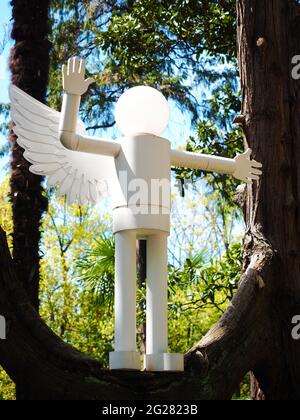 Decorative street lamp in the form of a white man with wings standing in pose on a tree branch Stock Photo