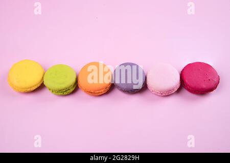 Lined up in a row of pastel-colored macaroons cookies on a pink paper background. Stock Photo