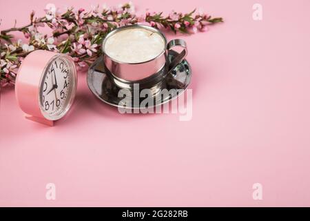 A cup of morning cappuccino with a pink alarm clock on a pink paper background. Stock Photo