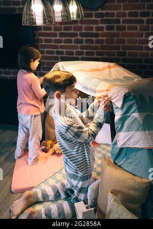 Boy helping little sister putting garland of lights in a tent for slumber party Stock Photo
