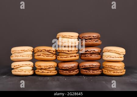 Brown, beige and cream colored French macarons stacked up in front of dark background Stock Photo