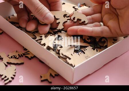 An open box with a wooden jigsaw puzzle close-up. Adult man and woman choosing a piece of a complicated puzzle. Active leisure. Logic games. Selective Stock Photo