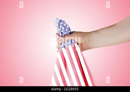 U.S. National Flag on a light red gradient background. Adult male holding the American symbol of freedom and independence in his hand. Side view. Stock Photo