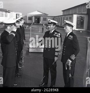 1960s, historical, outside at HMS Caledonia, in a hand-over of command, two Royal Naval Captains, one being introduced to a number of lower ranked officers, Fife, Scotland. Captain (Capt) is a senior officer rank of the Royal Navy, above a Commander and below Commodore and has a NATO ranking code of OF-5. The rank is equivalent to a Colonel in the British Army and Royal Marines, and to a Group Captain in the Royal Air Force. HMS Caledonia was first opened in 1937 and was responsible for artificer apprentice training up to 1985, with many thousands of young men going through training. Stock Photo