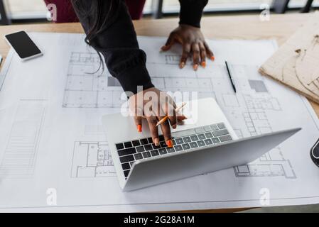 cropped view of african american female engineer using laptop near blueprint on desk Stock Photo
