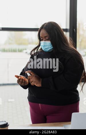 african american plus size businesswoman in medical mask applying sanitizer Stock Photo