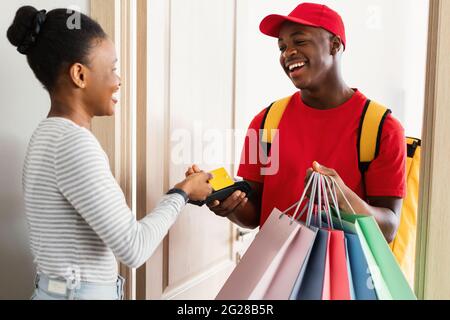 Cheerful Black Woman Paying Courier Using Credit Card At Home Stock Photo