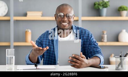 Happy mature african american man holding digital tablet and talking to camera, recording video, sitting at home office Stock Photo