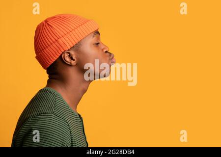 Profile Portrait Of Young Black Guy In Orange Hat Sending Air Kiss Stock Photo