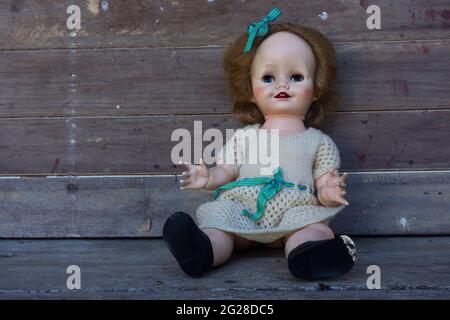 Scary creepy old vintage doll with staring eyes and blond hair in a knitted dress against a rustic background with copy space. Stock Photo