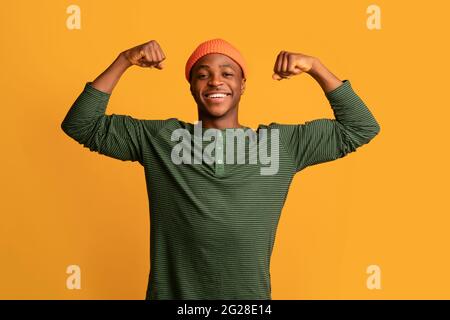 Strong Black Hipster Guy In Orange Hat Showing Biceps Muscles At Camera Stock Photo