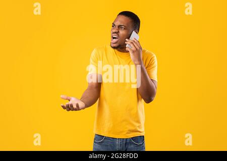 Furious African American Man Talking On Phone Over Yellow Background Stock Photo
