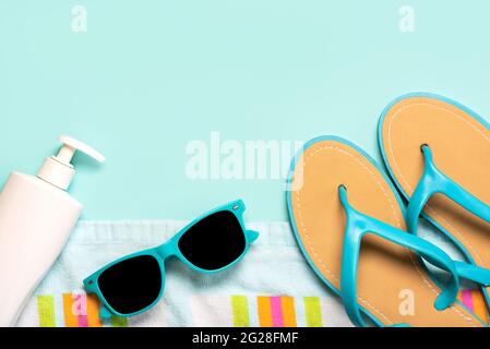 Summer holiday concept.Top view of blue flip flops,beach towel, blue sunglasses and bottle of sunscreen with copy space on a blue background Stock Photo
