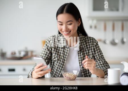 Positive asian woman having breakfast and surfing on social media Stock Photo