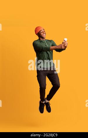 Cheerful African American Guy Using Modern Smartphone While Jumping In Air Stock Photo