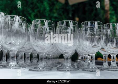 Many empty wine glasses in a line, close-up. Rows of empty wine glasses on the wedding table. Buffet in the open air. Catering background concept. Stock Photo