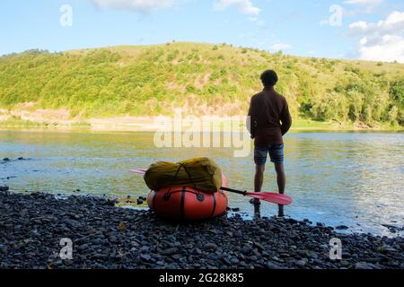 Tourist near yellow packraft rubber boat ready for adventures with red padle on a sunrise river. Packrafting. Active lifestile concept Stock Photo