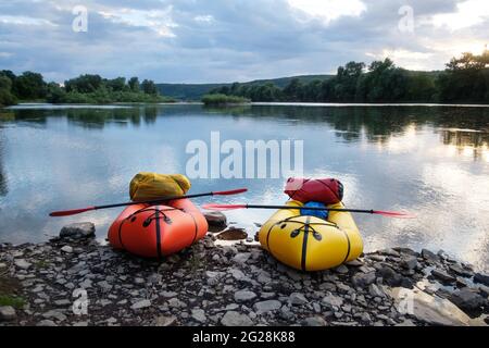 Orange and yellow packrafts rubber boats with padles ready for adventures on a sunrise river. Packrafting. Active lifestile concept Stock Photo