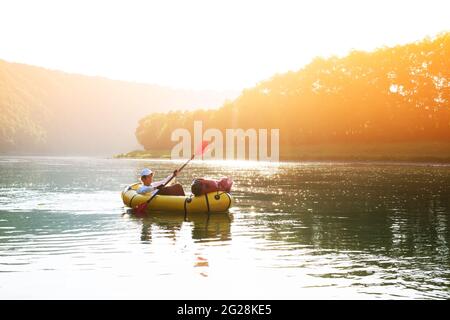 Tourist on yellow packraft rubber boat with red padle on a sunrise river. Packrafting. Active lifestile concept Stock Photo