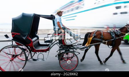 Havana, Cuba - 26 July 2018: Blurred wheels on a horse drawn carriage passing a cruise ship which is also blurry in Havana Cuba. Stock Photo