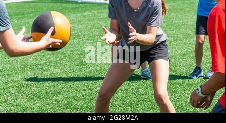 Young boys and girls are throwing and catching a medicine ball at practice during summer sports camp.