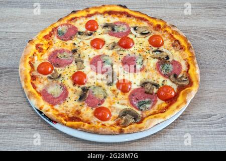 Delicious traditional Italian mozzarella pizza. From tomatoes, salami and mushrooms. In a plate, close-up from above. Stock Photo
