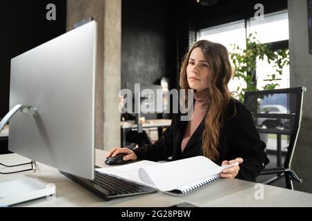 Design and architecture theme. A female young architect is working on a project with blueprints at the computer in a modern office. Architect engineer Stock Photo