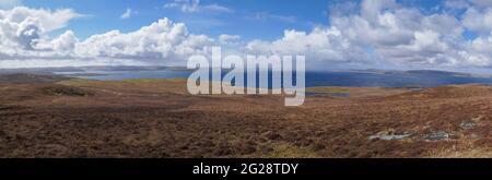 From the Hill of State on Lunna Ness, across open moorland, a panorama of Yell Sound on a sunny day with white clouds. Stock Photo