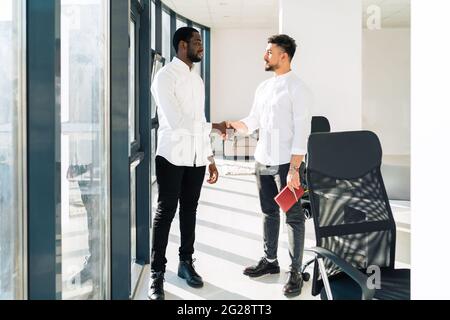 Two multiracial businessmen shake hands in office Stock Photo