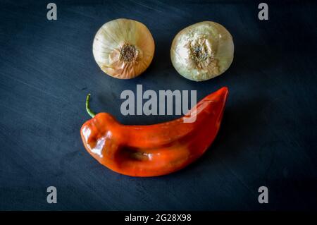 Two golden onions and one red sweet pointed pepper on a blackboard making an happy face close up Stock Photo