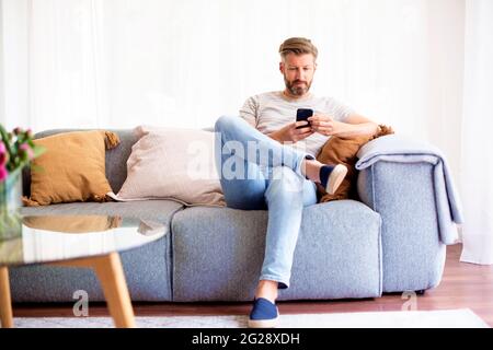 Shot of handsome man looking sitting on sofa at home and text messaging. Stock Photo