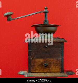 A beautiful old wooden coffee grinder against a solid red background Stock Photo