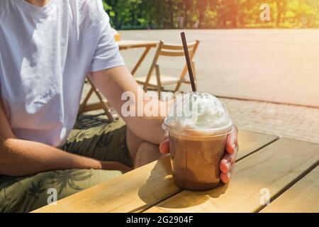 Man drinking iced coffee with whipped cream in street cafe. Stock Photo