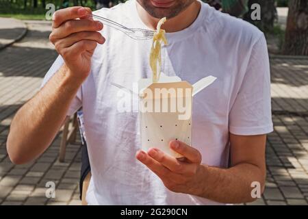 Close-up of man eating tagliatelle pasta from a paper box. Stock Photo