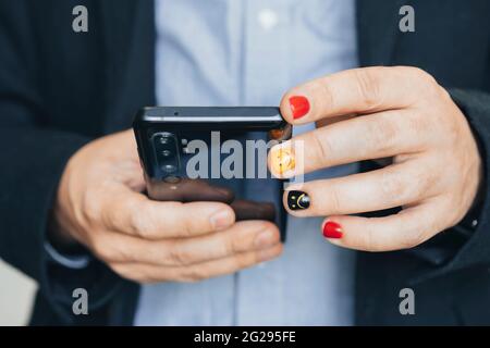 Close up of casual business man using mobile smart phone, reading business news update and marketing report via mobile app. Man with painted nails. De Stock Photo