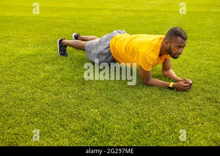 Side view of fit confident afro american athlete sportsman doing plank exercise on a grass field, young handsome male working out hard doing exercises Stock Photo