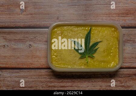Marijuana butter on wooden table with dark green leafs Stock Photo