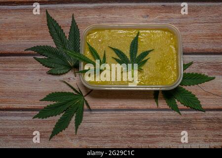 Marijuana butter on wooden table with dark green leafs Stock Photo