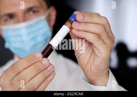 Test tube with blood sample in male hand close up. Doctor or scientist in mask with medical test Stock Photo