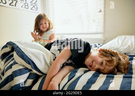 Portrait of smiling boy lying by sister on bed in bedroom at home Stock Photo