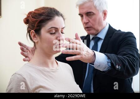 Mature gray-haired man hypnotizes Caucasian woman during hypnotherapy session. The psychologist uses alternative treatments for the subconscious mind Stock Photo