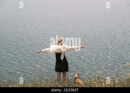 Woman next to a dog enjoying the sea scenery, arms spread. Going Stock Photo