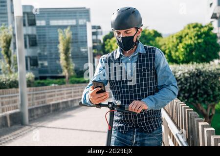 Young businessman standing on scooter and using smartphone Stock Photo