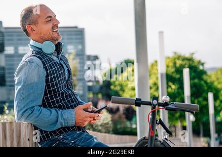 smiling businessman using the phone near an electric scooter. Stock Photo