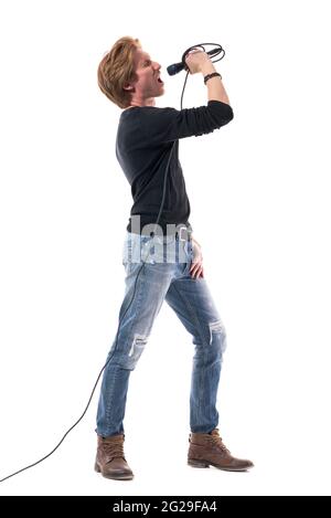 Loud energetic young singer singing loud and shouting on microphone. Full body length isolated on white background. Stock Photo