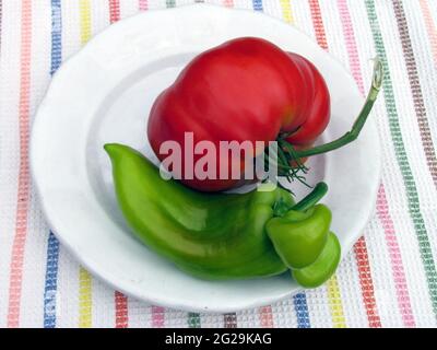 Huge tomato and atypically grown green pepper on white plate, fresh summer vegetables Stock Photo