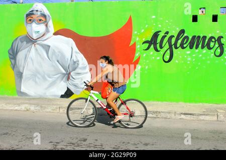 Mexican cyclist wearing a face mask passes in front of mural celebrating healthcare workers as Covid-19 Heroes, Merida Mexico Stock Photo