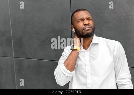 Overworking multitasking African American businessman freelancer entrepreneur standing outdoors. Tired and Exhausted having neck and headache after Stock Photo