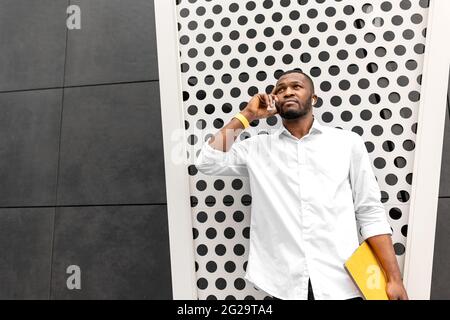 Serious young african american business man freelancer in casual trendy clothing professional making business call on the phone outdoors looking up Stock Photo