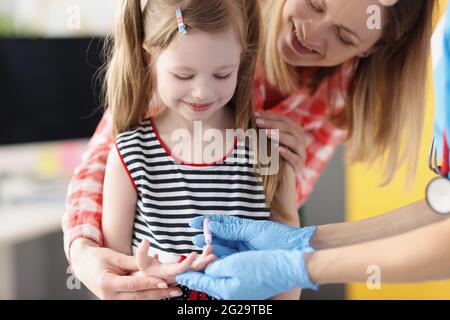 Doctor laboratory assistant taking blood of little girl using lancet in clinic Stock Photo